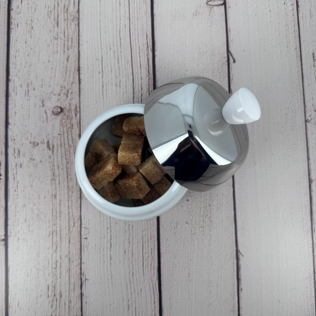 Discover the Salam white porcelain sugar bowl by Degrenne, paired with a mirror-polished steel lid, filled with cane sugar cubes.